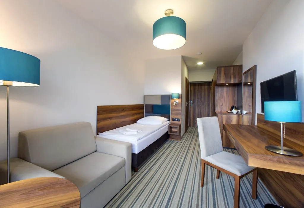 Pokój jednoosobowy w Solina Resort w Polańczyku z sofą, biurkiem i turkusowymi lampami