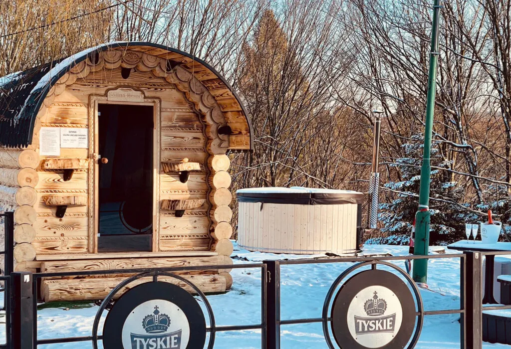 Drewniana sauna w kształcie beczki i balia na zewnątrz w Solina Resort zimą, w tle ośnieżone drzewa