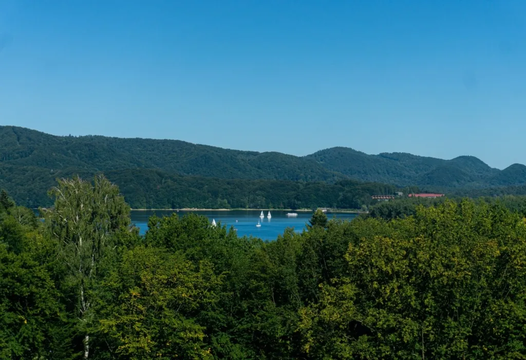 Panorama Jeziora Solińskiego z żaglówkami i zalesionymi wzgórzami